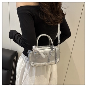 Detail of silver metallic Boston bag featuring white lace trim and metal bow accent