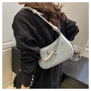 Detail of light blue glossy crescent bag with pearl chain and bow charm on a model