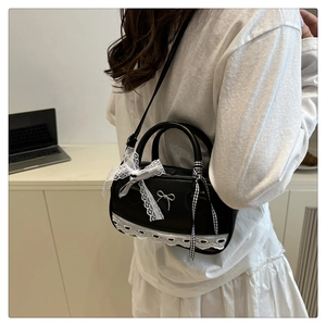 Detail of black Boston bag with white lace trim, bows, and plaid ribbon on model