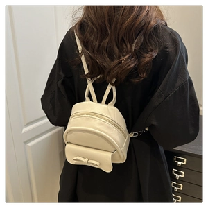 On-body shot of a mini cream white backpack with a bow detail and metal zippers