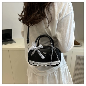 Detail view of black matte leather Boston bag with delicate white lace and metallic bow