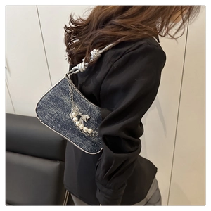 Detail der dunkelblauen Denim-Achseltasche mit silbernem Schmetterling und Perlenkette