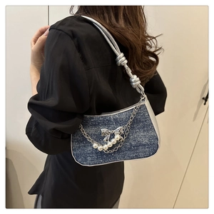 Detail of denim shoulder bag with silver bow accent and elegant pearl chain strap