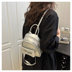Mini silver metallic backpack with bow detail shown on model in a modern indoor setting