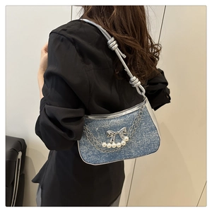 Detail view of denim shoulder bag with silver bow, pearls, and chain on a female model