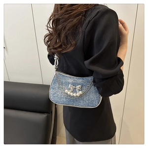 Détail d'un sac sous le bras en jean avec papillon argenté et décor de perles blanches
