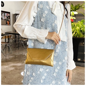 Detail of gold envelope crossbody bag with crinkle texture and thin chain strap