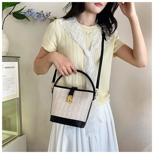 Detail of woven straw bucket bag with black leather trim and golden metal swivel lock closure