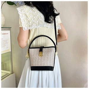 Detailed view of woven straw bucket bag with black leather trim and golden lock clasp