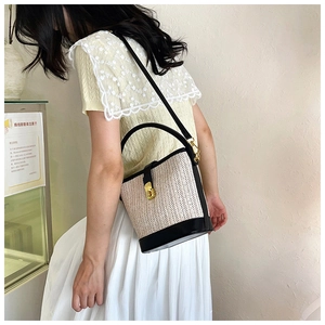 Detail of woven bucket bag with black leather trim and elegant golden twist lock clasp