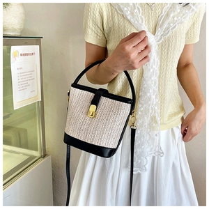 Detail of woven straw bucket bag featuring black leather trim and gold twist-lock closure