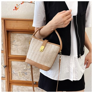 Detail of handwoven straw bucket bag with brown leather trim and golden metal lock