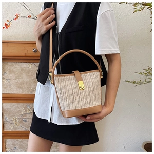 Detail of woven straw bucket bag with brown leather trim and golden metal clasp