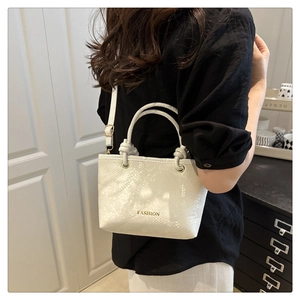 Detail of white snake-textured bucket bag with gold lettering and knotted handle