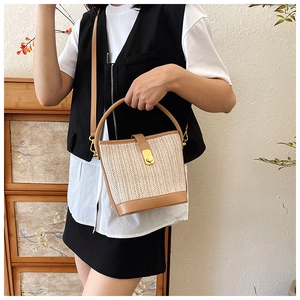 Close-up of woven straw bucket bag with brown leather trim and golden metal hardware