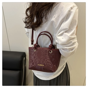 Detail of burgundy snakeskin texture crossbody bag worn by model in a cozy setting