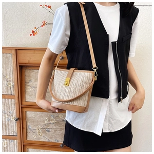 Detailed shot of straw woven bucket bag featuring brown leather trim and golden metal lock