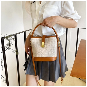 Detail of woven bucket bag featuring brown leather trim and golden metal clasp closure