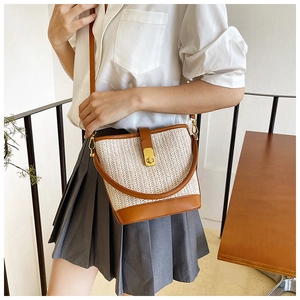 Detail of woven straw bucket bag featuring brown leather trim and golden metal twist lock