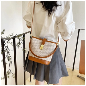 Detail of woven straw bucket bag with brown leather trim and gold twist lock closure
