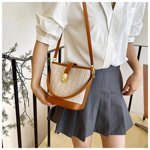 Detail of woven straw bucket bag with brown leather trim and golden metal clasp