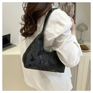 Détail d'un sac porté épaule noir à motif serpent porté par un mannequin au bureau