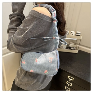 Detail of light blue denim shoulder bag with pink floral rose and bow print textures