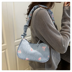 Detail of blue denim shoulder bag with floral print and ruched strap on a model