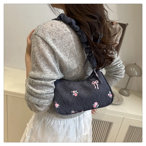 Detail of blue denim hobo bag featuring pink floral embroidery and pleated shoulder strap