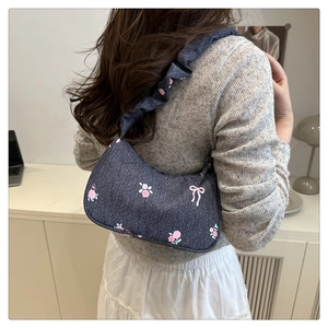 Detail of crescent shoulder bag with floral embroidery and ruffled strap on model