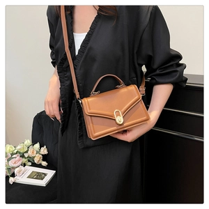 Close-up of a brown leather shoulder bag with a gold metal buckle on a model