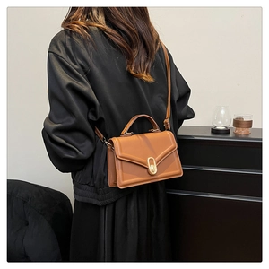 Sac bandoulière en cuir marron avec fermoir tournant doré porté à l'épaule du mannequin