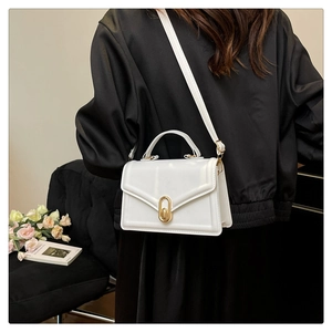 Detail of white structured crossbody bag with gold oval clasp on a black outfit