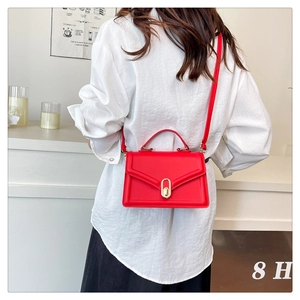 Detail of a bright red trapezoidal handbag with gold lock and adjustable shoulder strap