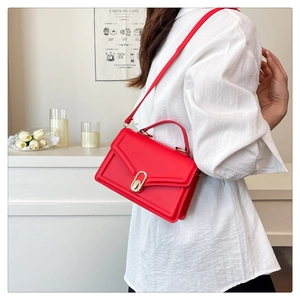 Detail of red leather envelope crossbody bag with gold hardware and top handle strap