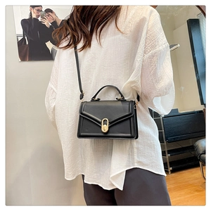 Detail of black leather crossbody bag featuring a gold oval clasp and round top handle