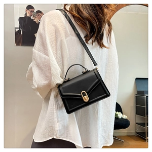 Detail of a black leather square bag featuring a gold oval clasp and crossbody strap