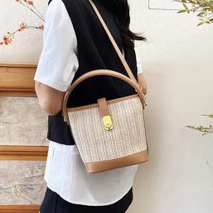 Woven straw bucket bag with brown leather trim shown in a natural lifestyle setting