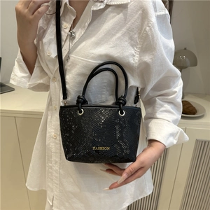 Sac seau noir texture serpent avec doubles poignées et bandoulière dans un décor élégant