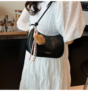 Detail van zwarte lederen halve maan tas met pluche beer hanger en gevlochten touw accent