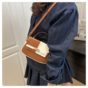 Detail of contrast color crossbody bag with gold hardware shown on a model's denim outfit