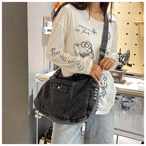 Detail der dunkelgrauen Messenger-Tasche aus gewaschenem Denim mit Pattentaschen und Fransen
