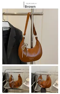 Détail d'un sac hobo marron avec un charm nœud en perles argentées et détails de logo