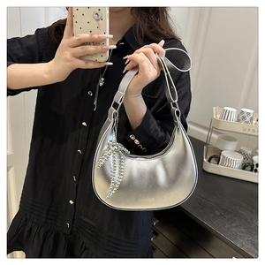 Detailed view of silver metallic crescent bag with bow charm and Fashion logo