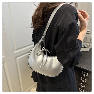 Detail of silver crescent moon shoulder bag featuring a beaded bow and metallic finish