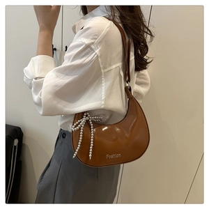 Close-up of brown glossy crescent bag with silver Fashion metal logo and bead bow charm