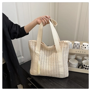 Close-up of cream woven tote bag with canvas handles and a stylish tassel charm