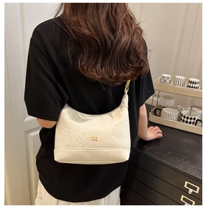 Detail of white snakeskin texture on a crescent shoulder bag with gold lettering