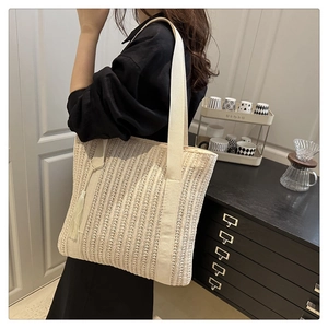 Detail of a large beige straw woven tote bag with fringe charm and fabric shoulder strap