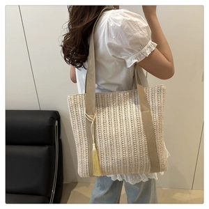 Detail of woven straw tote bag with long tassel charm and durable canvas strap